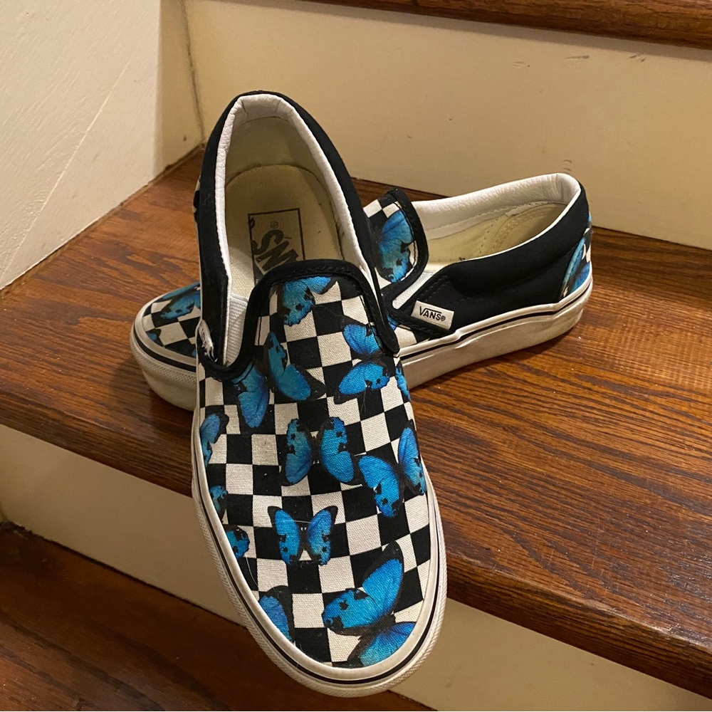 Black and white checkered slip on Vans with blue butterflies